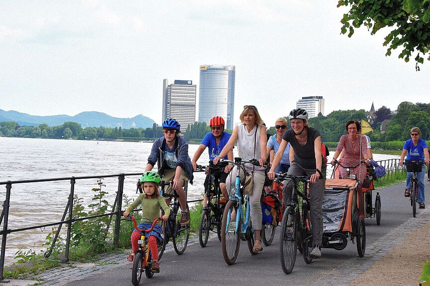 Fahrradfahrende am Bonner Rheinufer, im Hintergrund Siebengebirge, Posttower und Langer Eugen