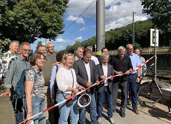 Bürgermeister und andere Leute stehen auf dem zu eröffnenden Rheinradweg und schneiden mit der Schere ein Band durch